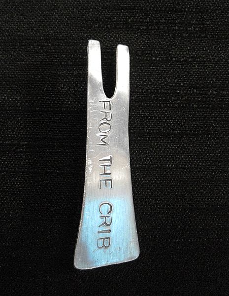 From the Crib: Aluminium  brooch,  Black Singlet shape, stamped with the words "FROM THE CRIB" $50